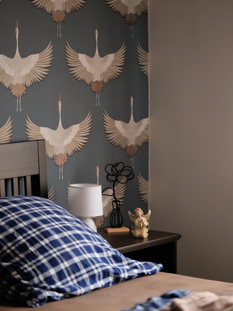 Bedroom wall papered with a flying-crane motif in slate blue, beside a bedside lamp