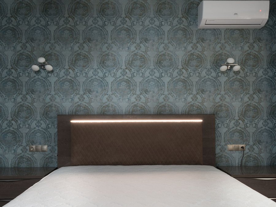 Teal damask wallpaper covering the wall behind an upholstered bed with a concealed light strip
