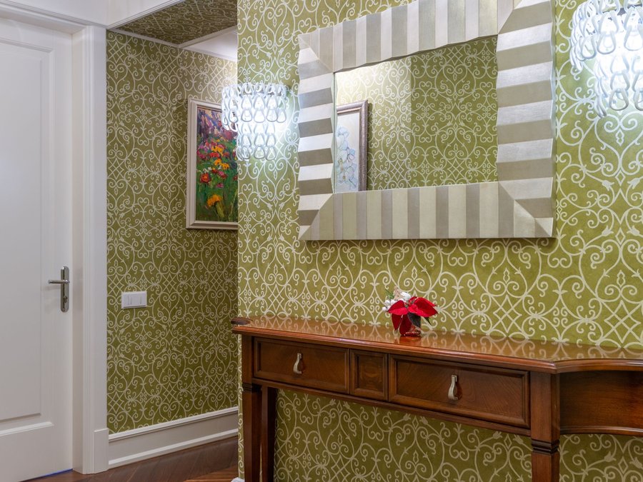 Hallway papered in olive-green damask, with a dark wooden console table and a framed mirror