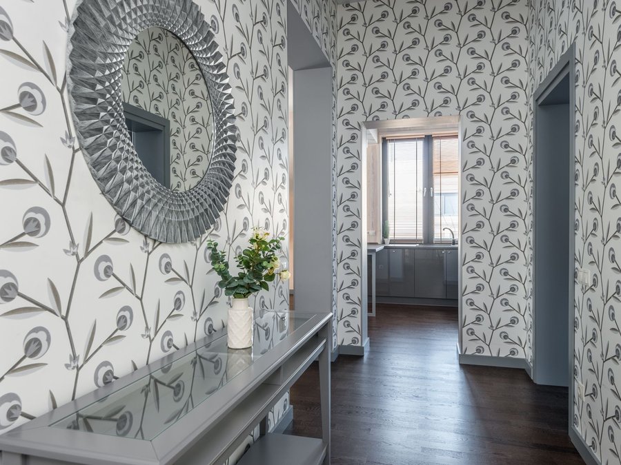 Hallway papered in a grey feather print, with a console table and round mirror