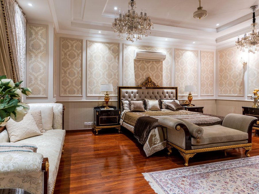 Formal bedroom with gold damask wallpaper set into moulded wall panels and a chandelier above